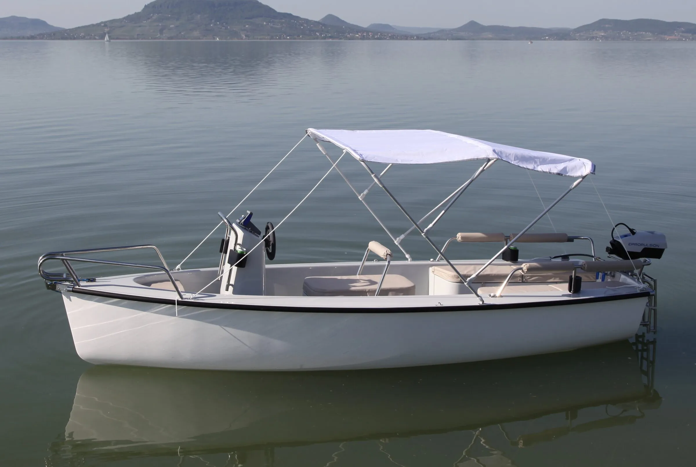 Fehér elektromos csónak bimini tetővel a Balatonon, háttérben a Badacsony